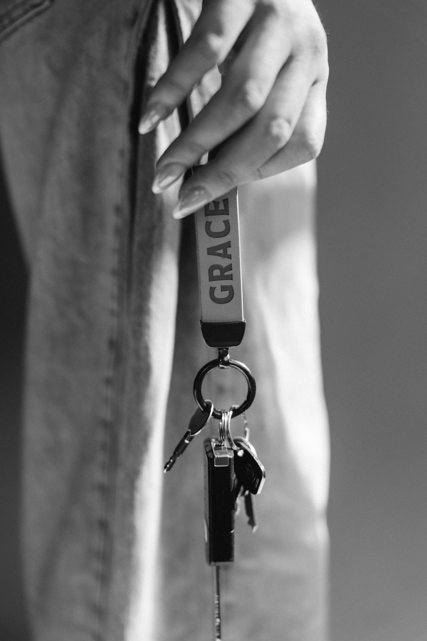 A hand holding a set of keys on a keyring printed with the word GRACE, black and white.