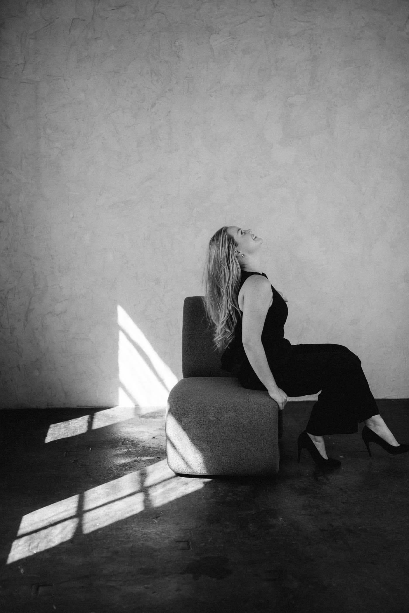 A woman seated in a pool of window light, face turned up, black and white.